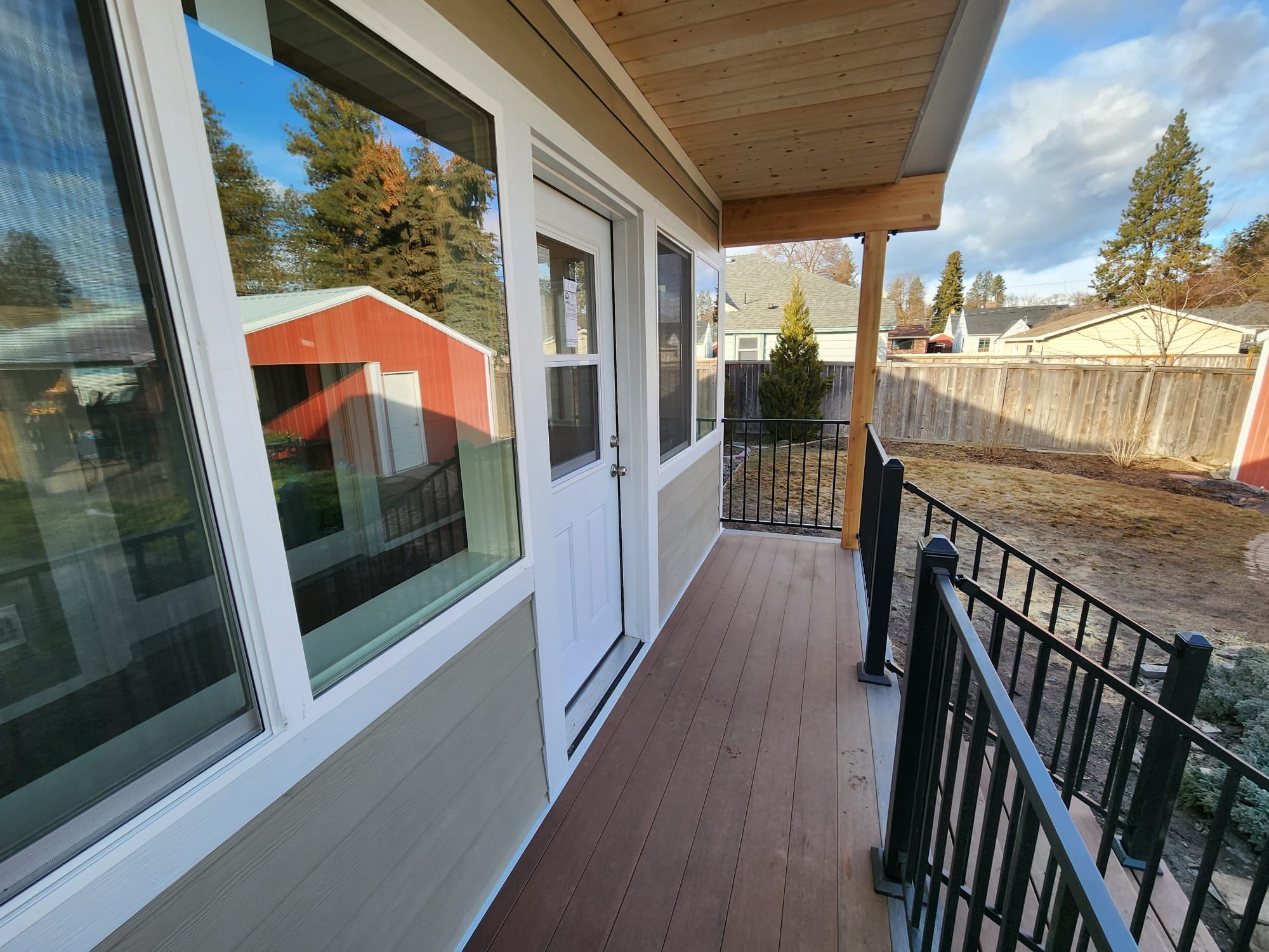 Porch beside enclosed room with white door, angled windows, brown composite floor, black railing, red barn beyond