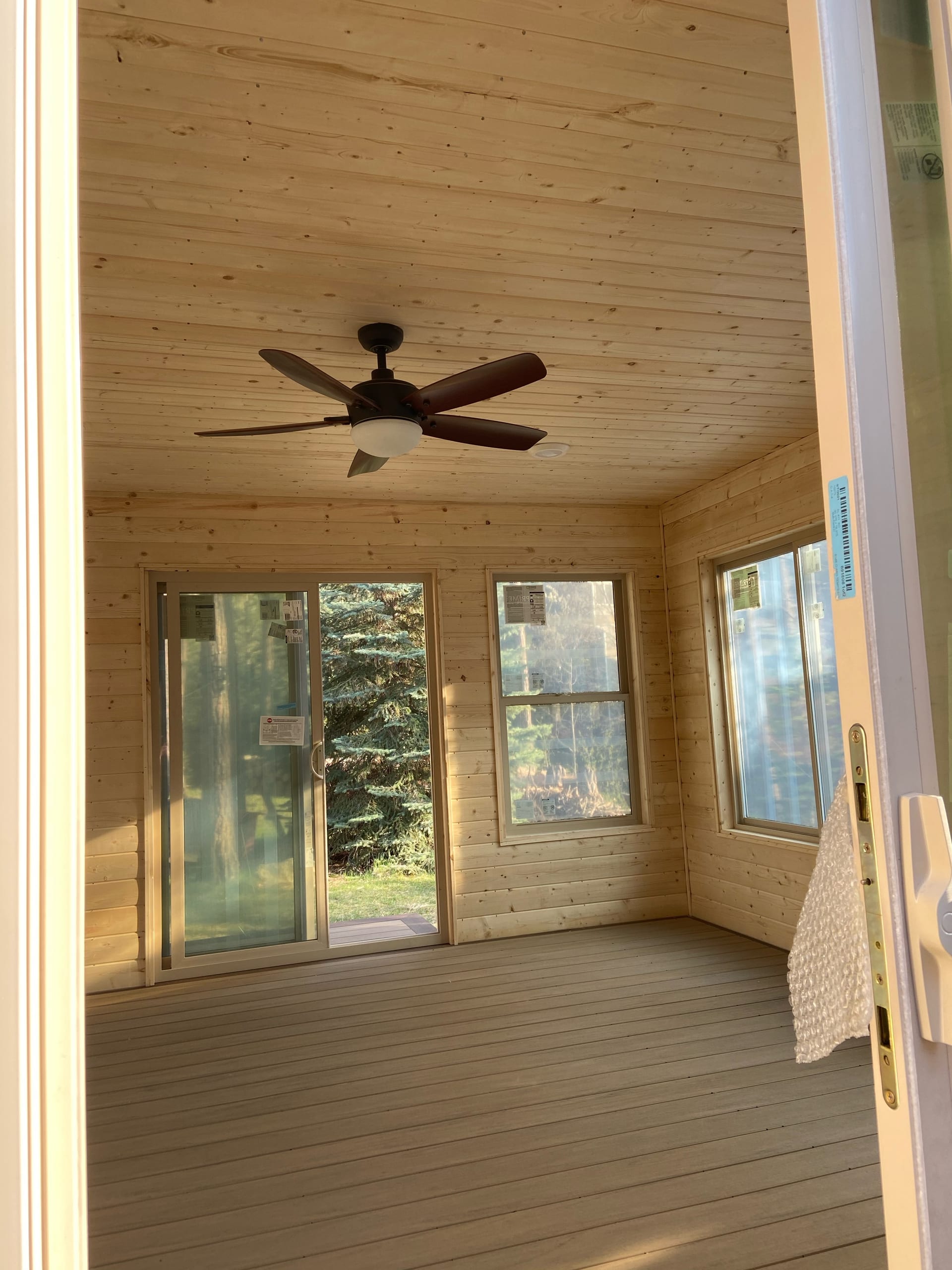 Portrait of enclosed sunroom with pine ceiling and ceiling fan, windows on three sides, open sliding door