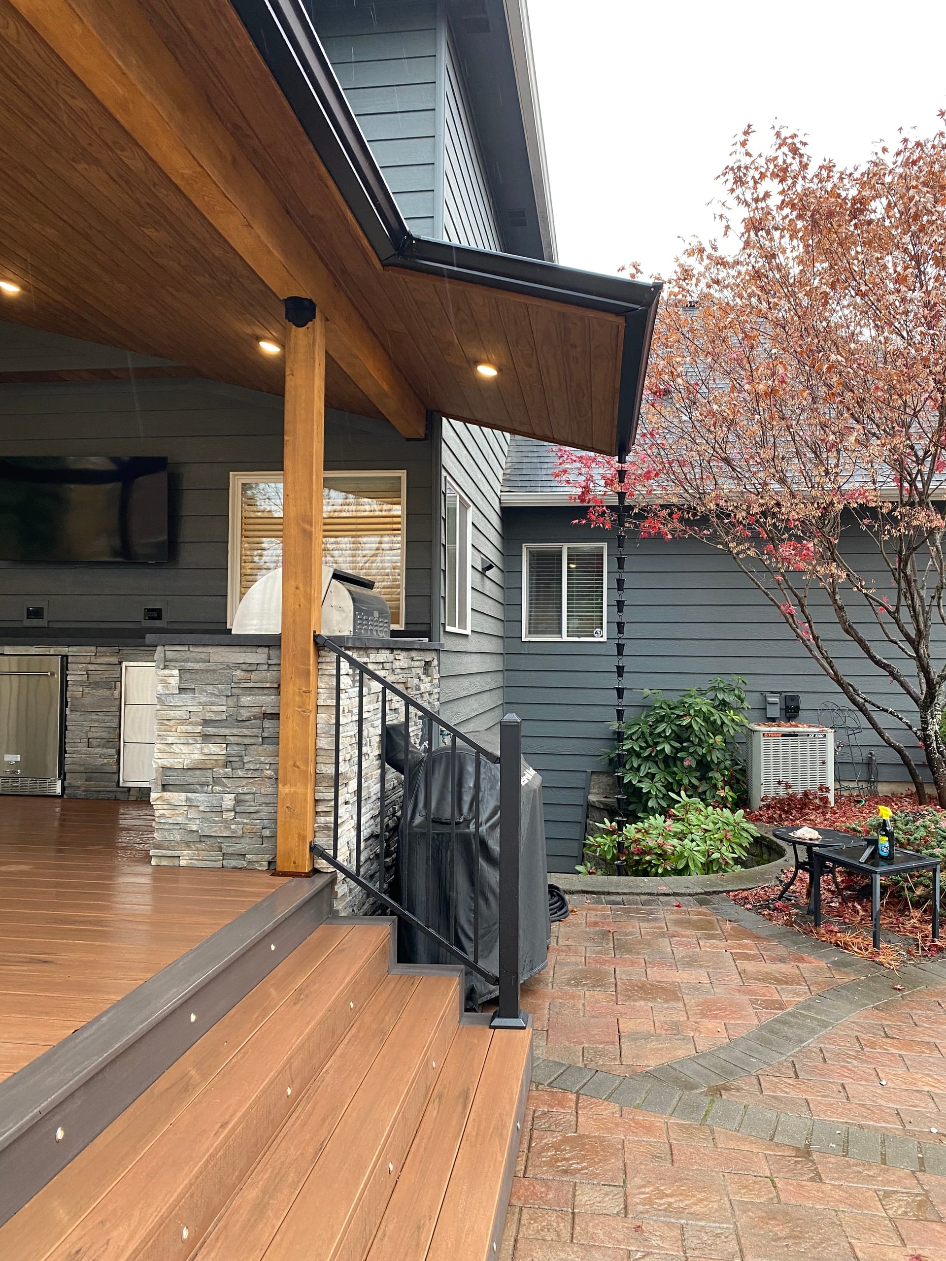 Portrait view from step landing into covered deck with stained post, recessed lights, kitchen and railing