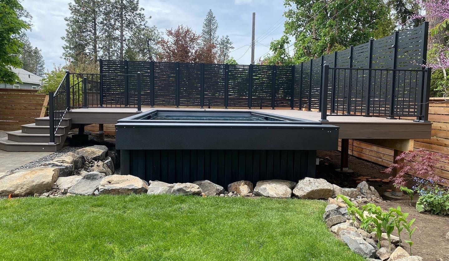 Raised pool deck with black steel surround, screen fence and lawn with rock edge