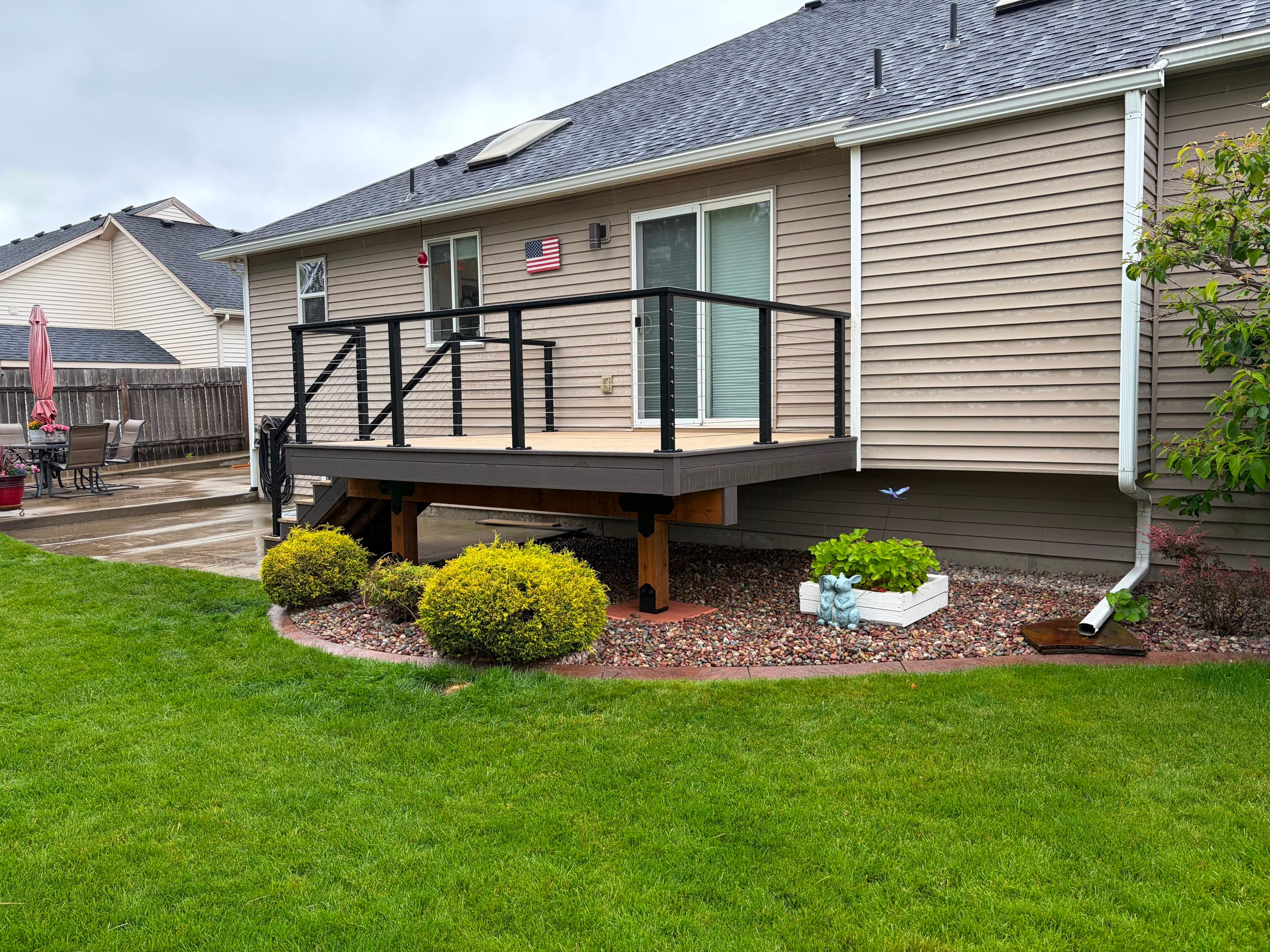 Raised tan deck with black cable railing and stairs beside a landscaped rock bed
