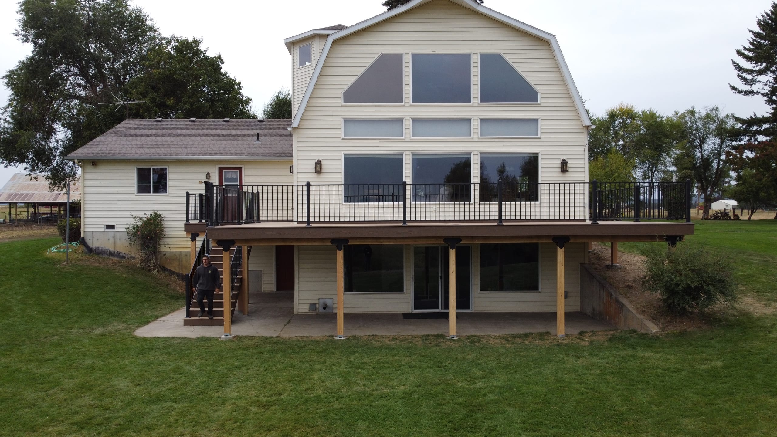 Rear view of long elevated brown composite deck with black railing on white house with large arched windows