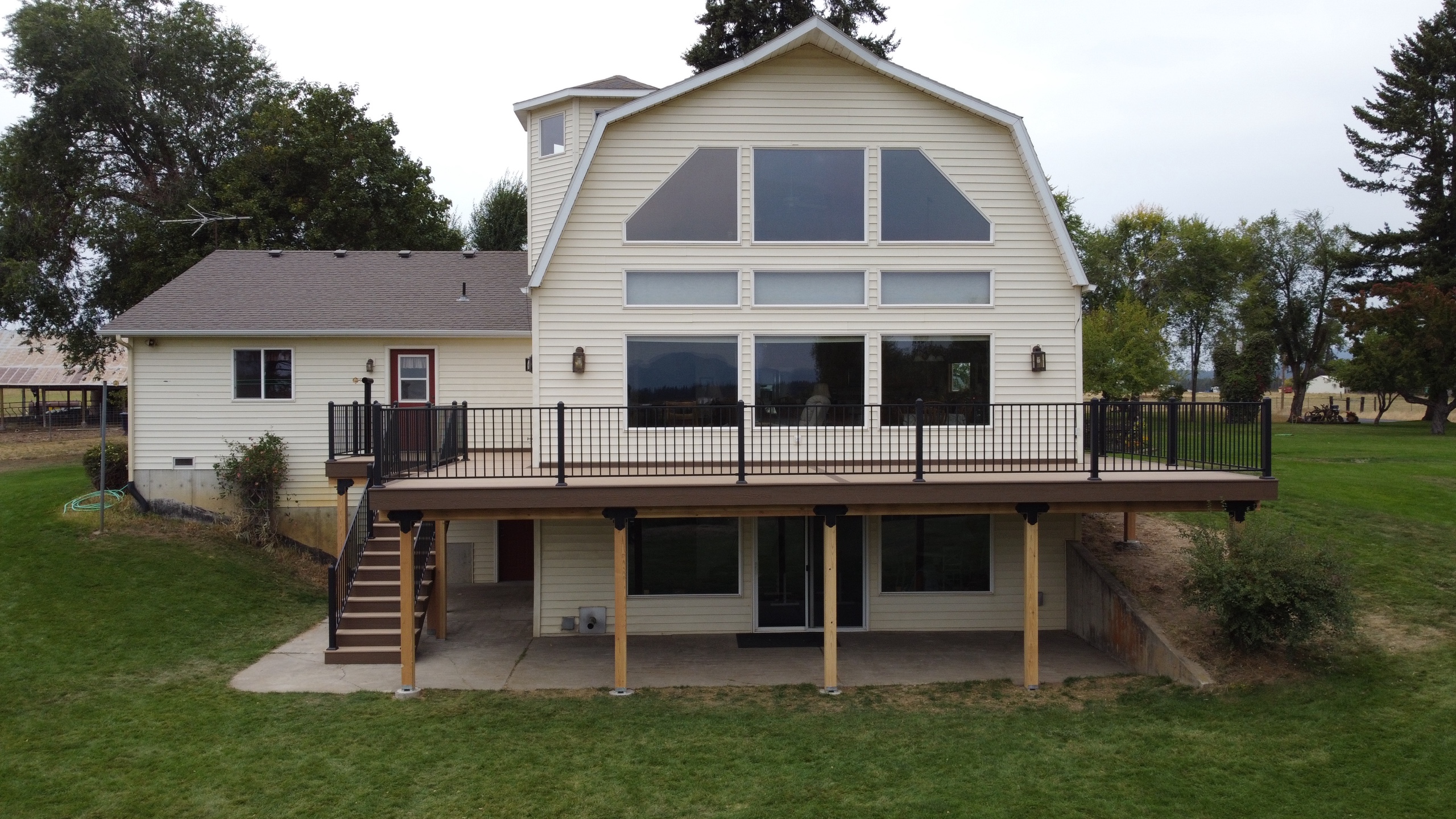 Rear view of white gambrel house with long brown composite deck, black railing and cedar posts, stairs at left