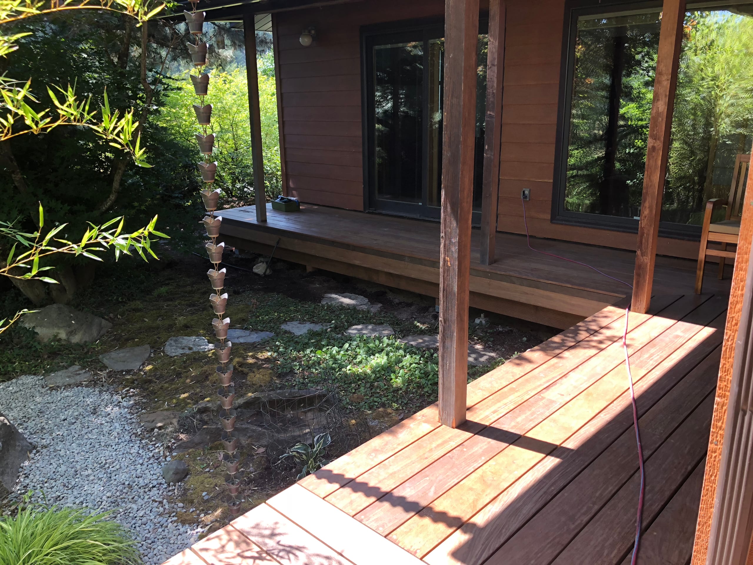 Red-brown hardwood deck and covered porch at a modern cabin with gravel and landscaping, shade shadows