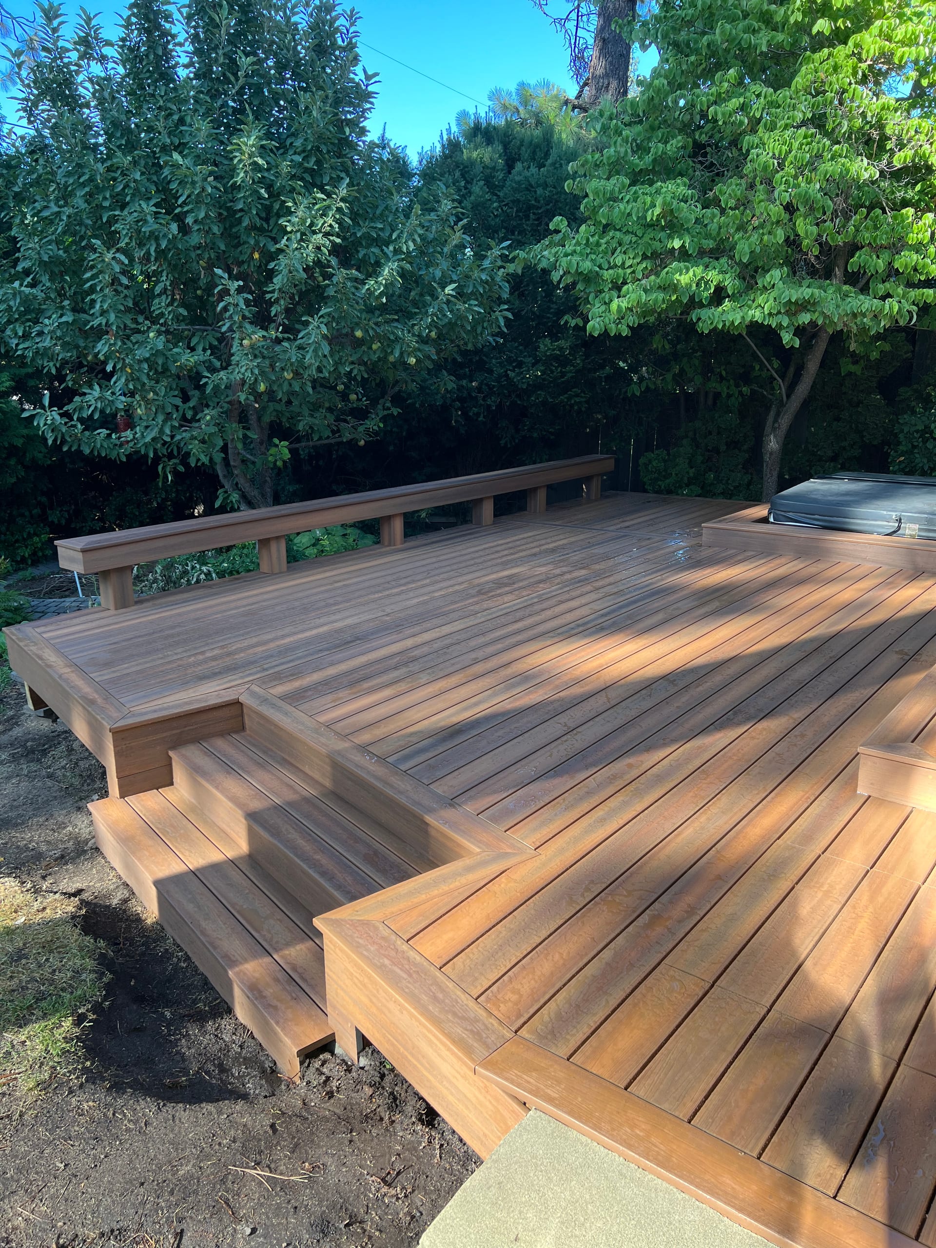 Red-brown hardwood ground-level deck with steps and perimeter bench in a leafy yard