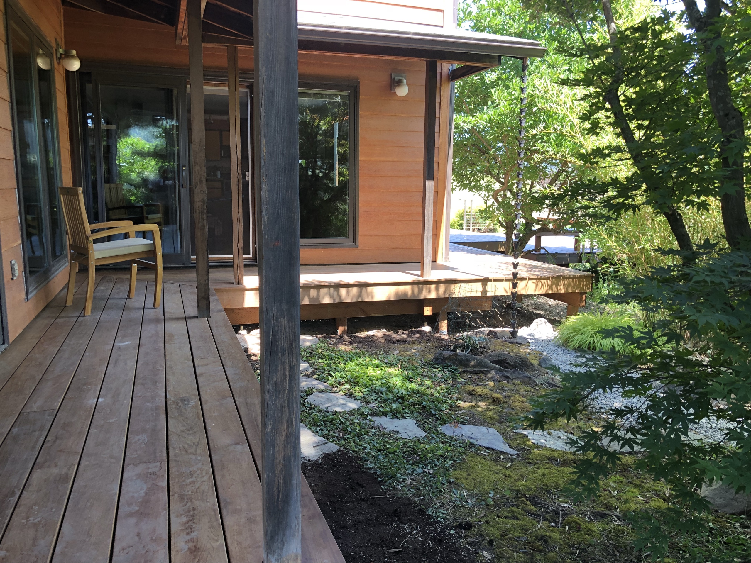 Red-brown hardwood porch deck at a modern cabin with chair, stepping stones and garden