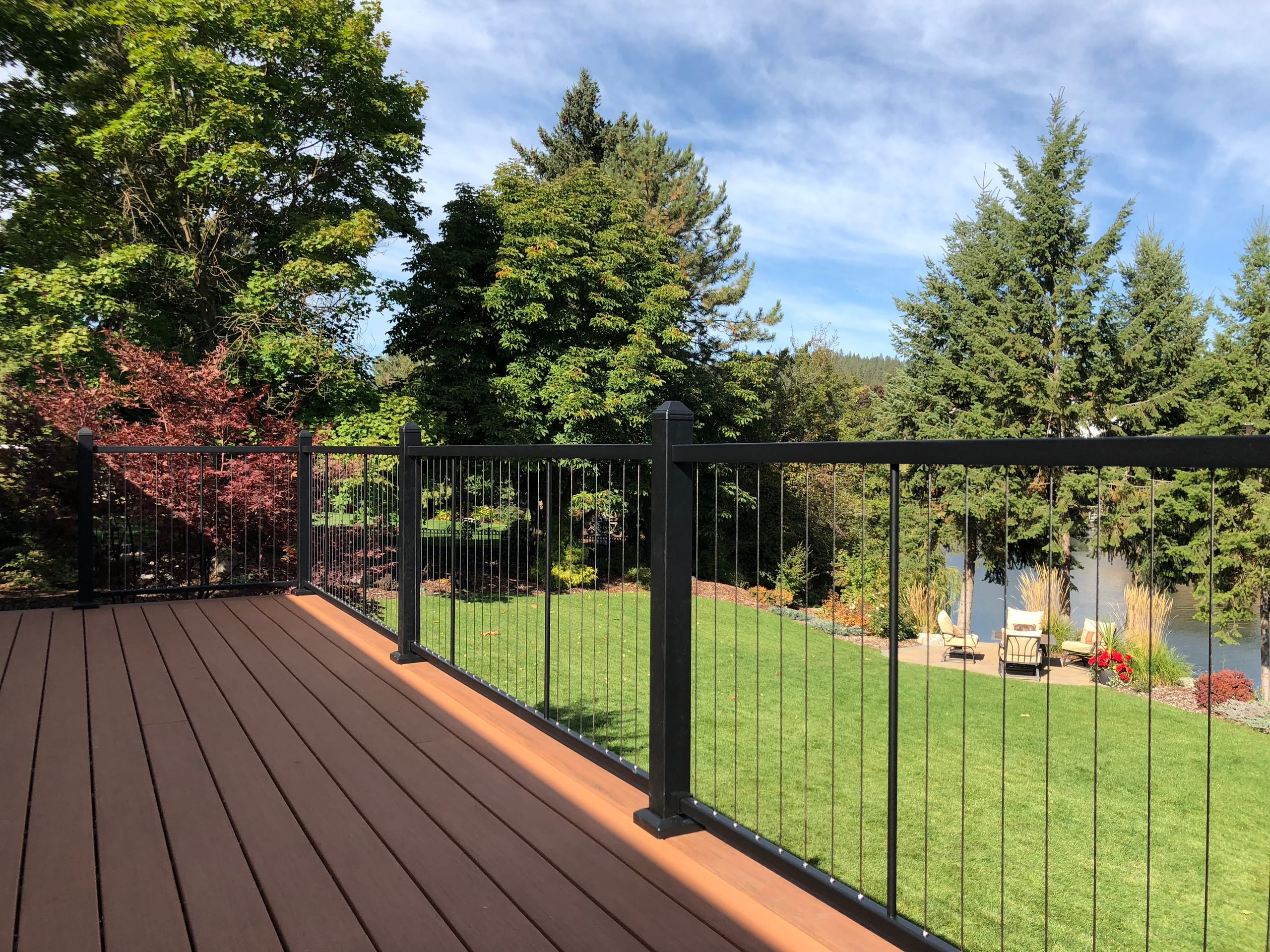 Reddish-brown composite deck with black cable-style railing and trimmed lawn with trees