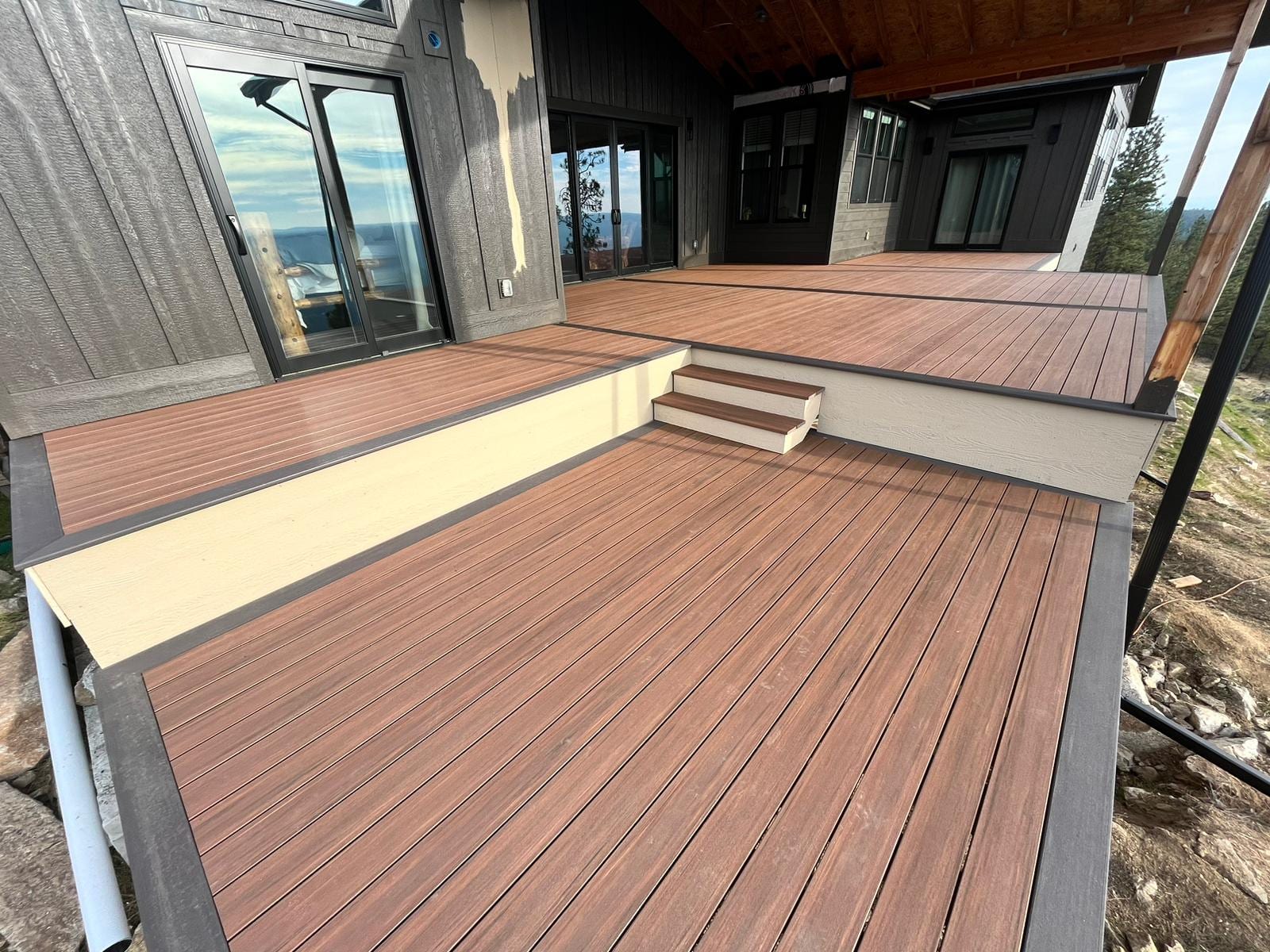Reddish-brown composite deck with dark border, cream riser step and upper level at a dark house with covered porch