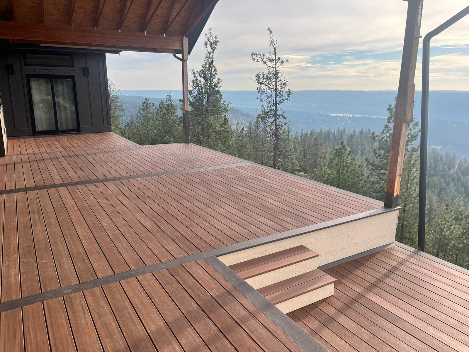 Large reddish-brown deck with gray border boards and built-in steps overlooking a forested valley
