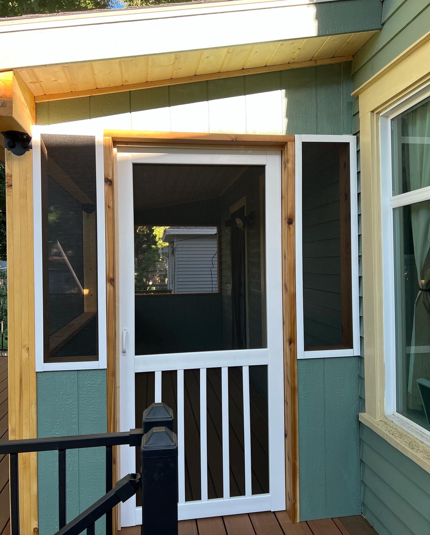 Screened porch entry with white screen door and green siding, stained wood fascia, black railing post