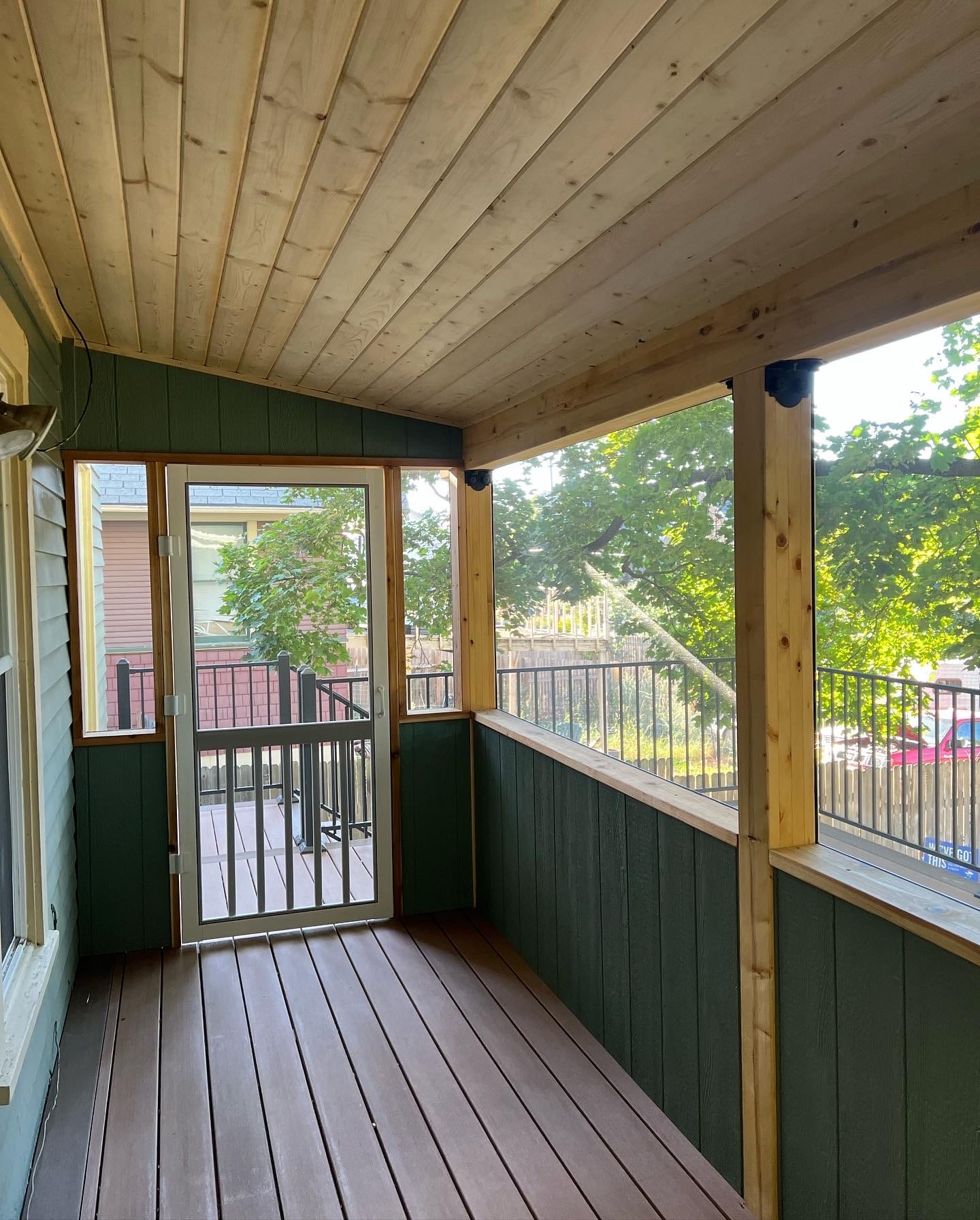 Inside a screened porch with wood plank ceiling, green walls and screen door