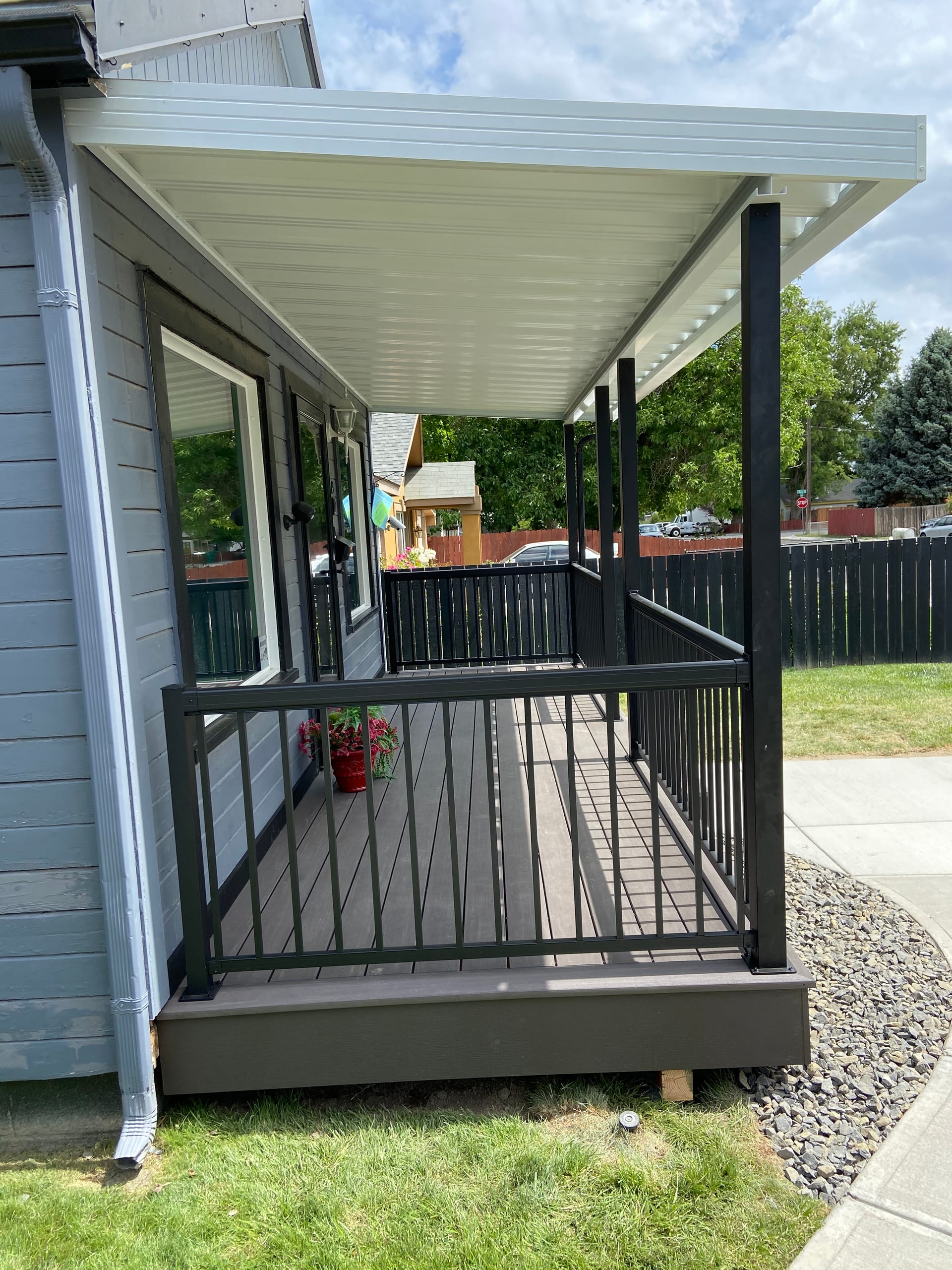 Side view of covered porch with white roof, dark composite deck and black railing on grey house