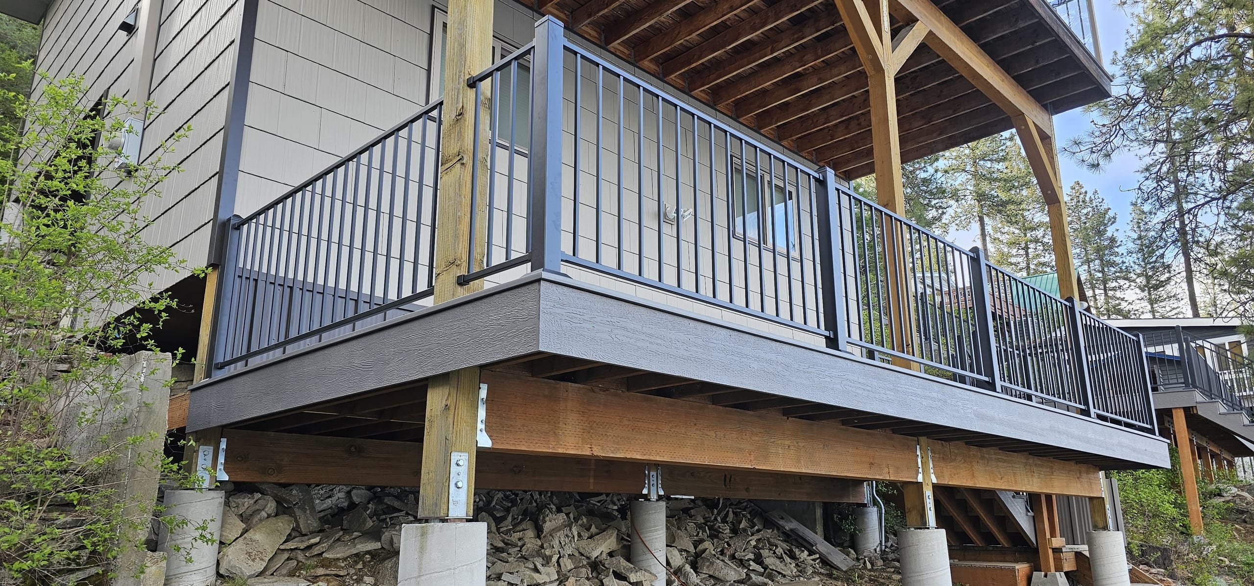 Side view of raised gray composite deck with black metal picket railing on timber posts and concrete piers with a gabled cover above