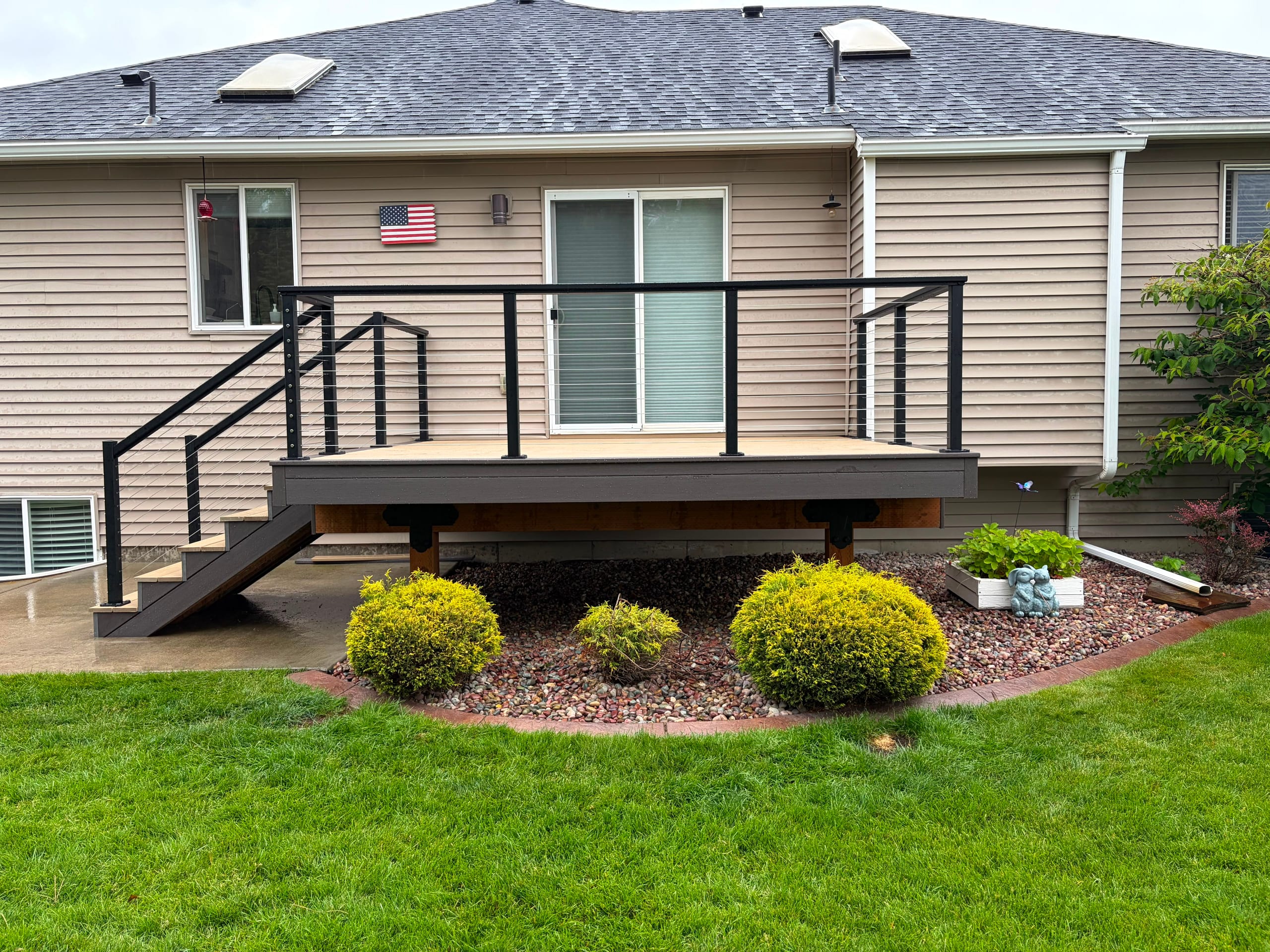Small raised deck with tan decking and black cable railing at the back of a house