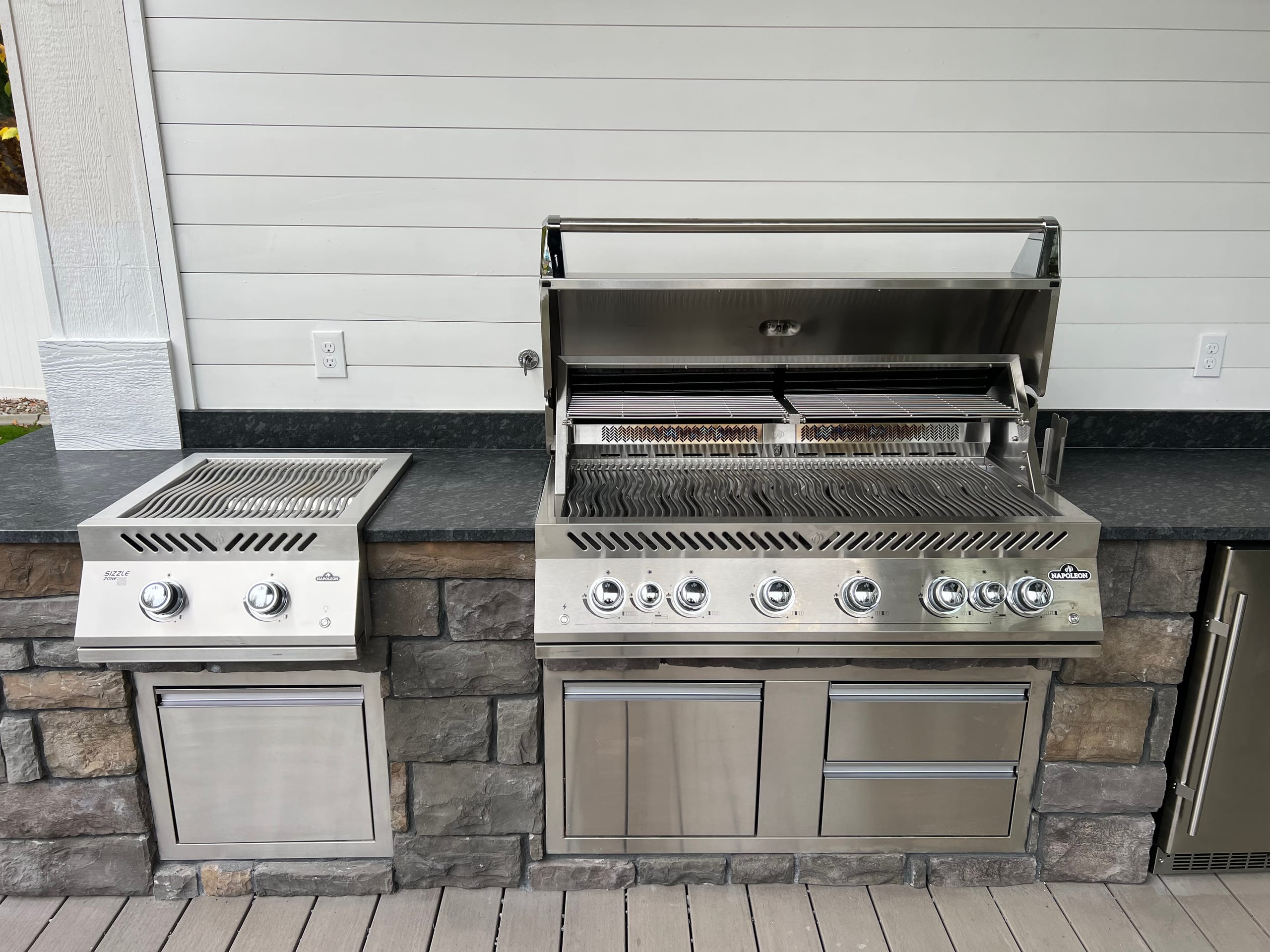Stainless grill and side burner set in stone veneer base with drawers, white siding behind