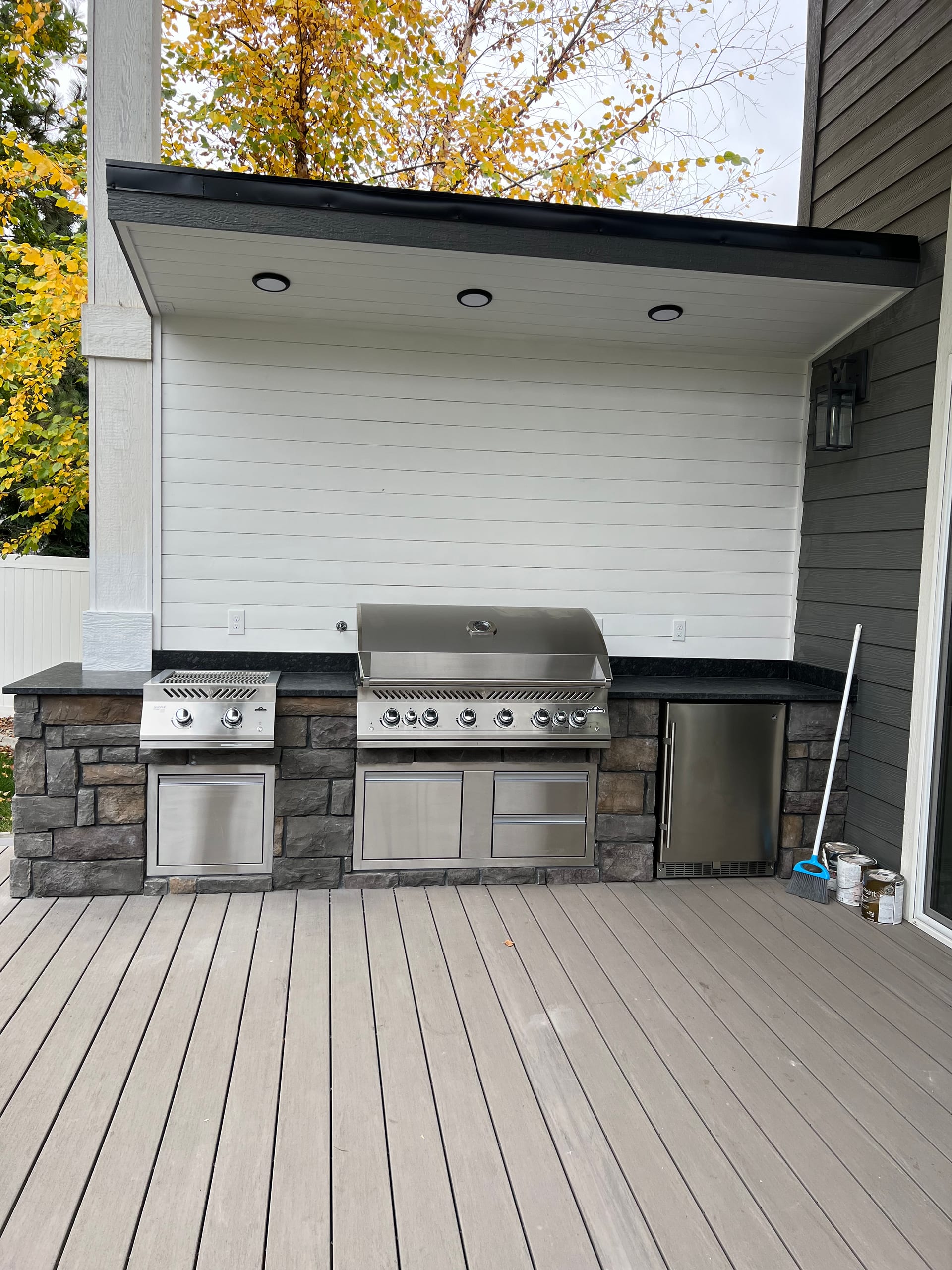 Stone-clad outdoor kitchen with built-in grill under recessed-light canopy on gray composite deck