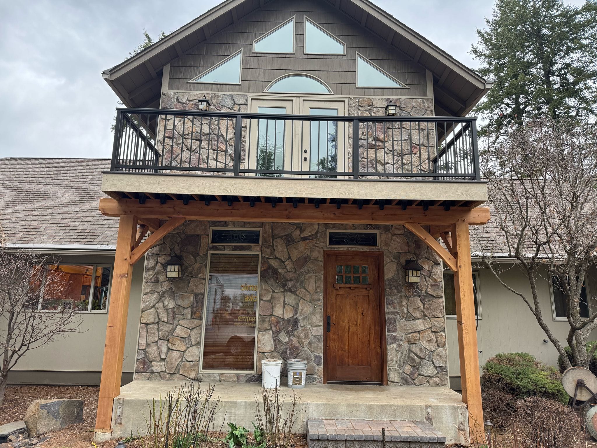 Stone-faced entry with timber-framed porch roof supporting an upper balcony with black railing, two-story chalet home
