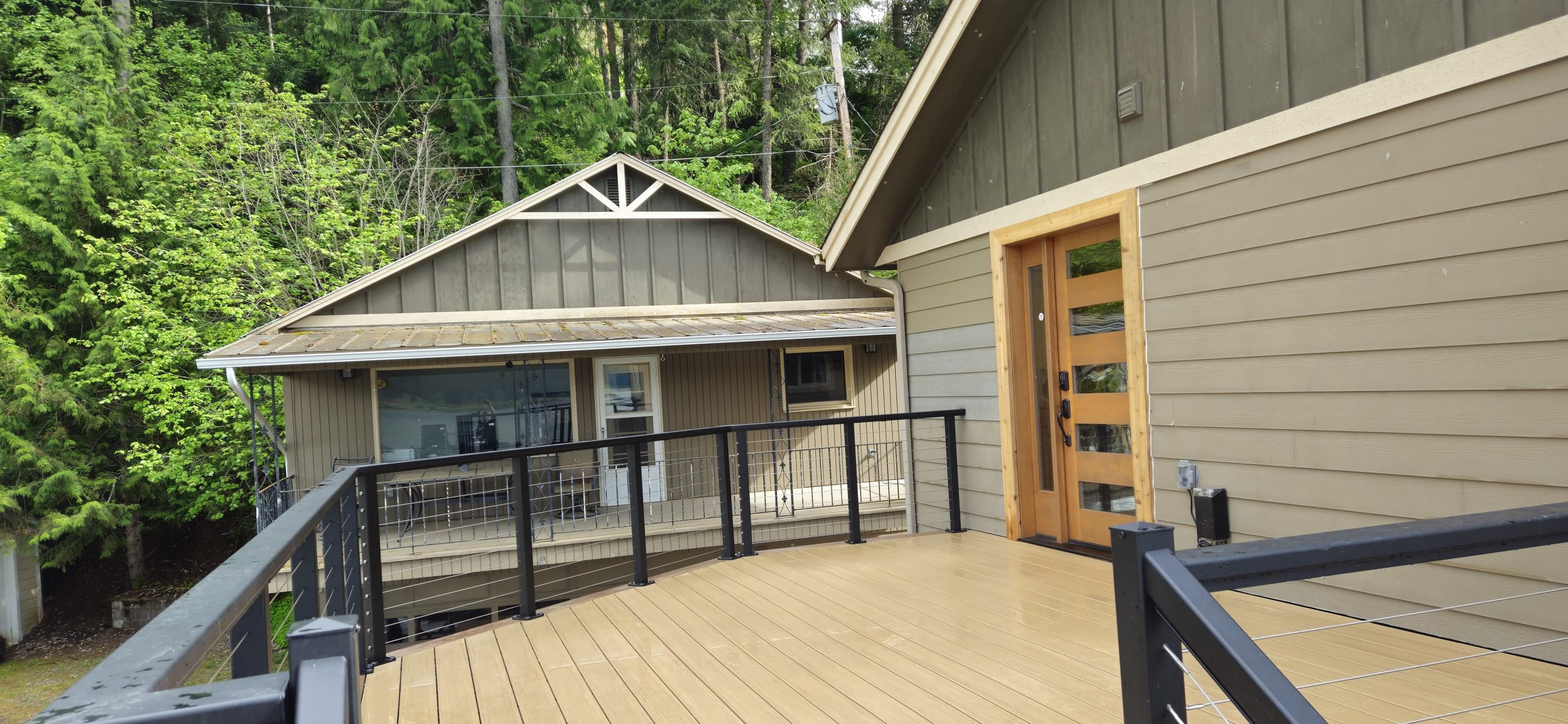 Tan composite deck with black cable railing leading to a modern front door on green-gray craftsman house