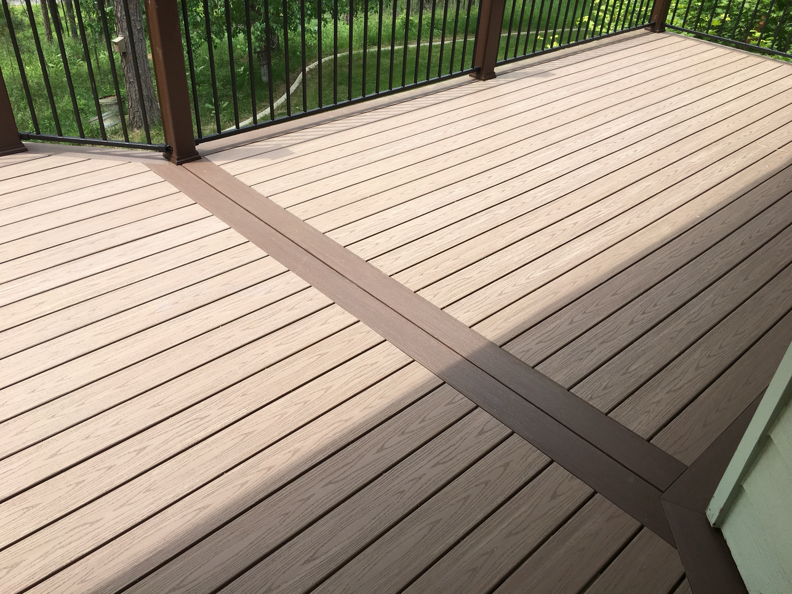 Tan composite deck with brown border inlay and black picket railing under a roof overhang