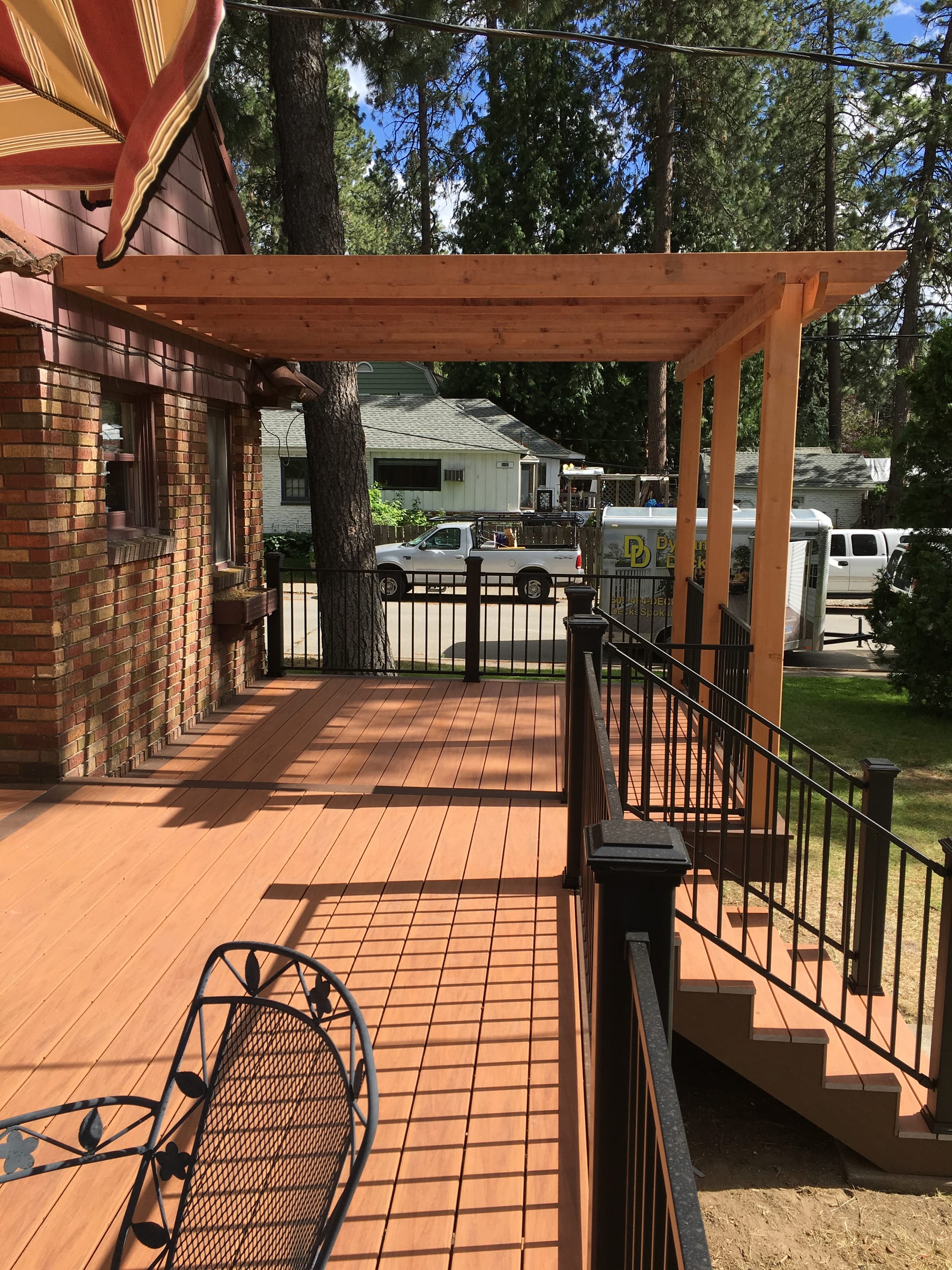 Terracotta composite deck with black picket railing and stairs next to a cedar pergola on a brick house