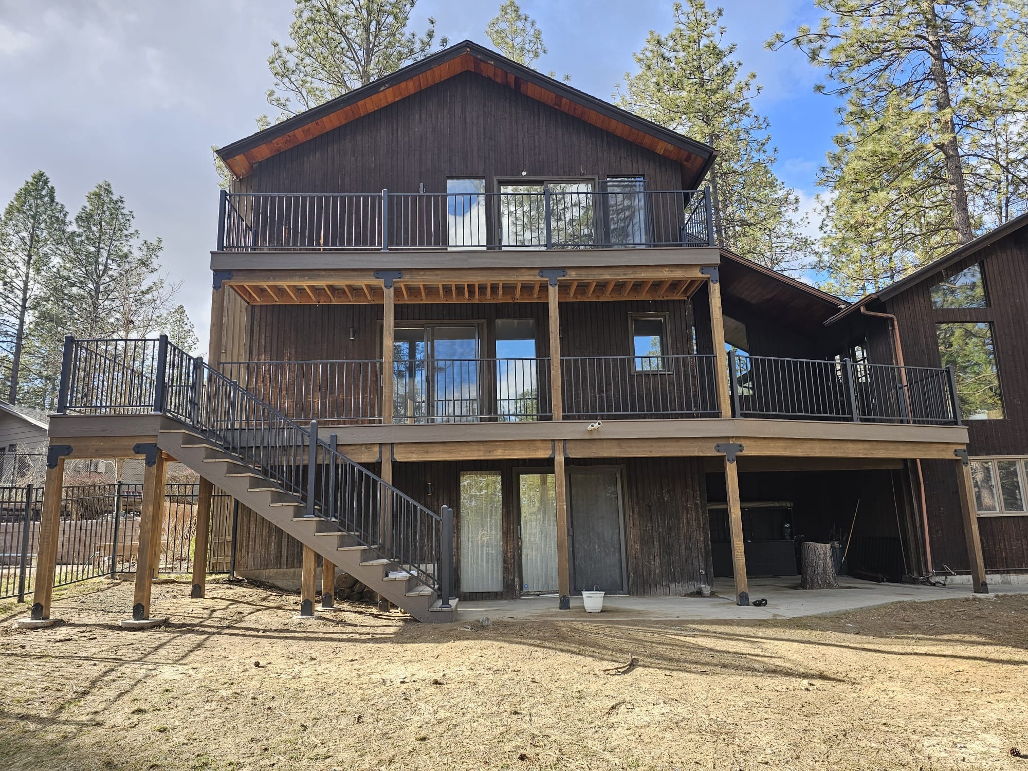 Three-story home back with two stacked decks, wood railings and long staircase on posts, bare yard