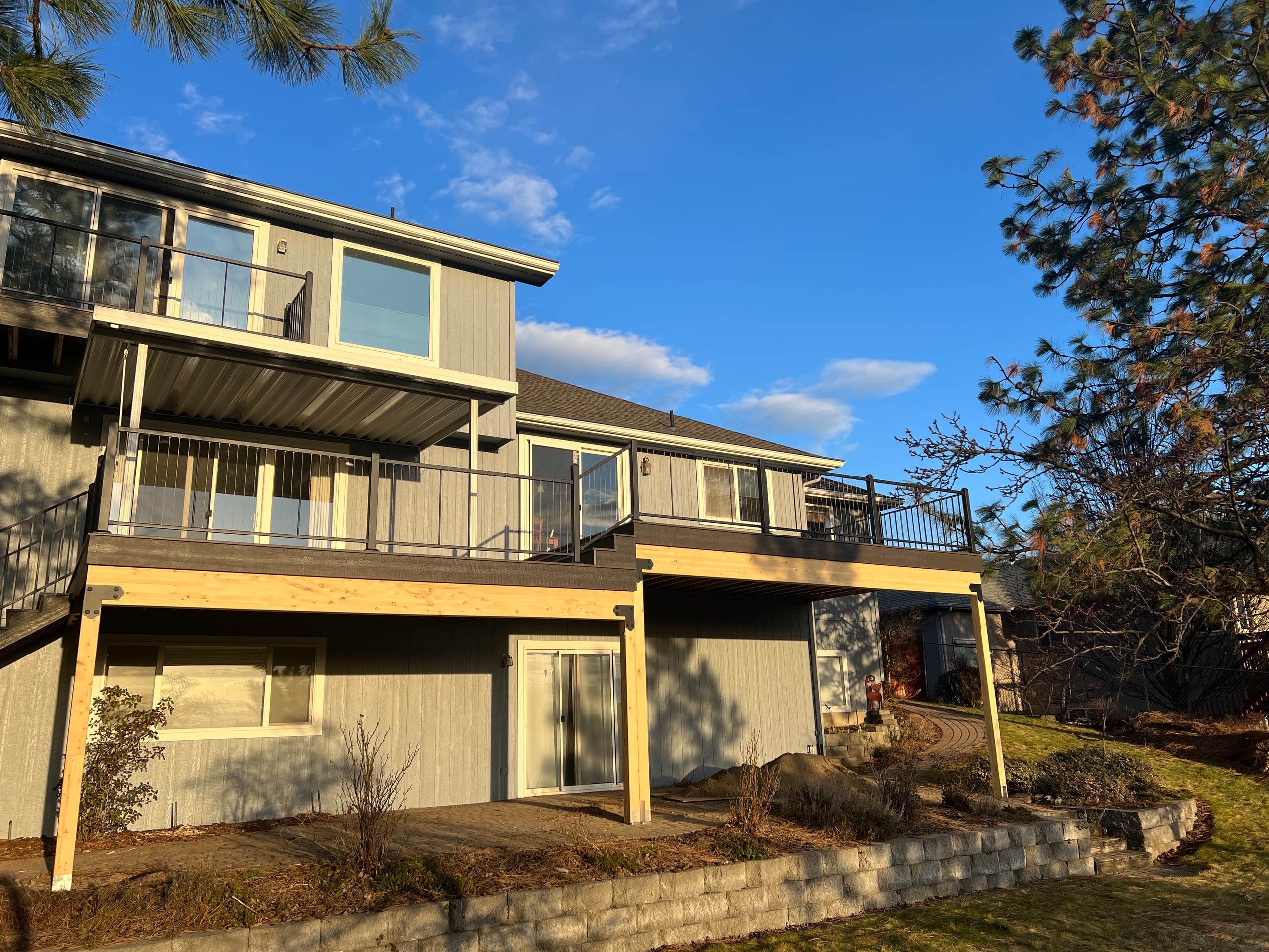 Two-level house with upper deck and glass railing over an insulated cover and lower deck, stone retaining wall