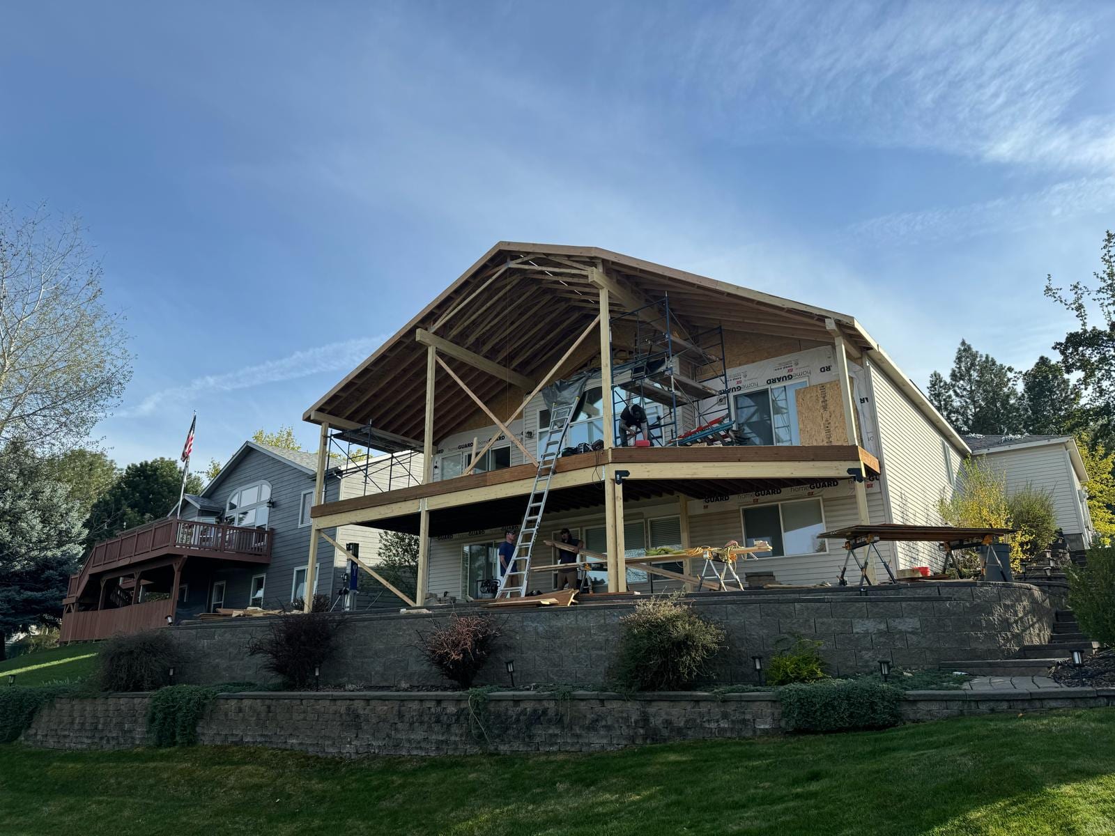 Two-storey lakeside-style house with large upper deck being rebuilt, open timber roof framing and scaffolding