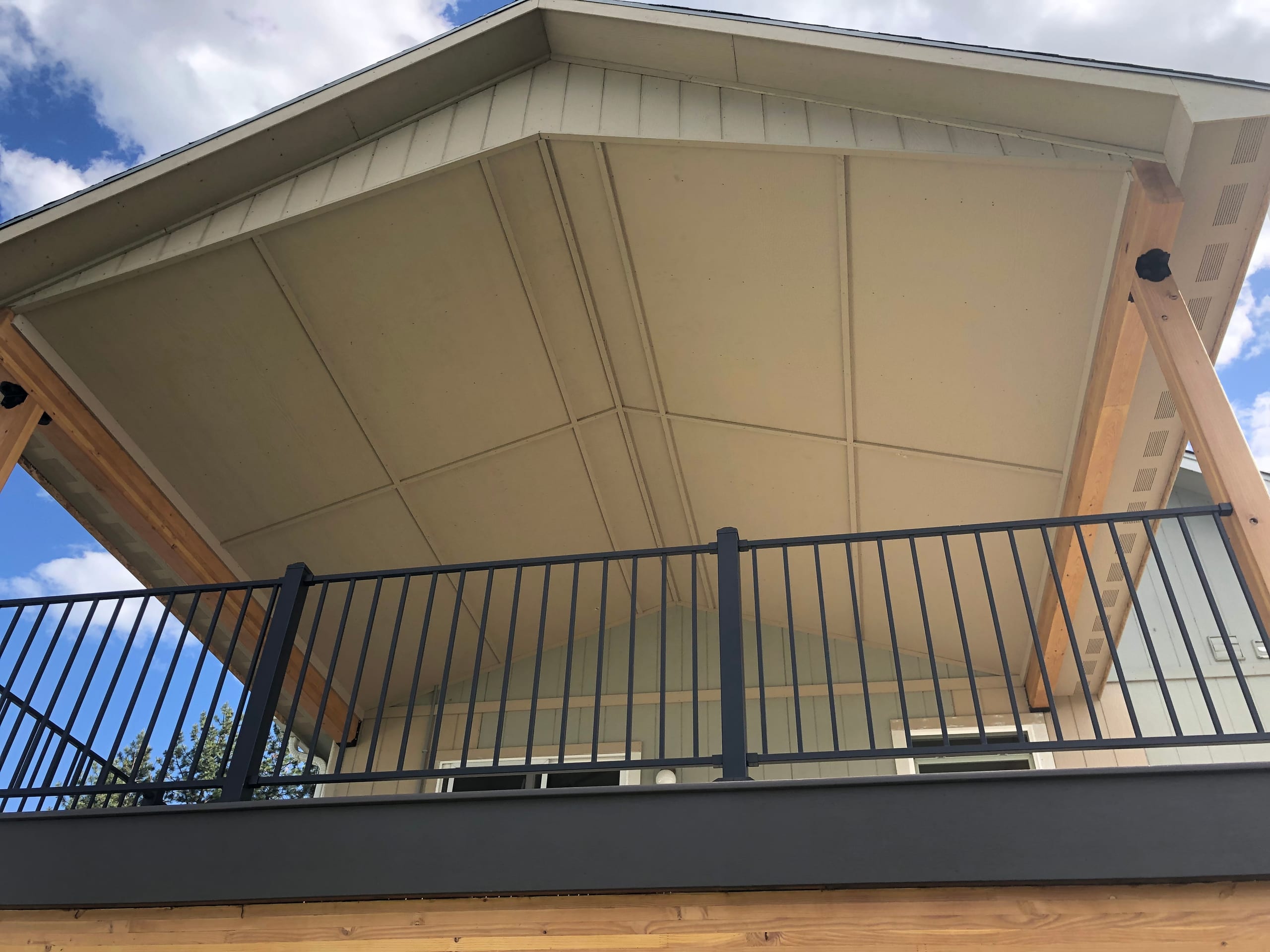 Underside of gabled deck roof cover with cedar rafters, black railing and blue sky