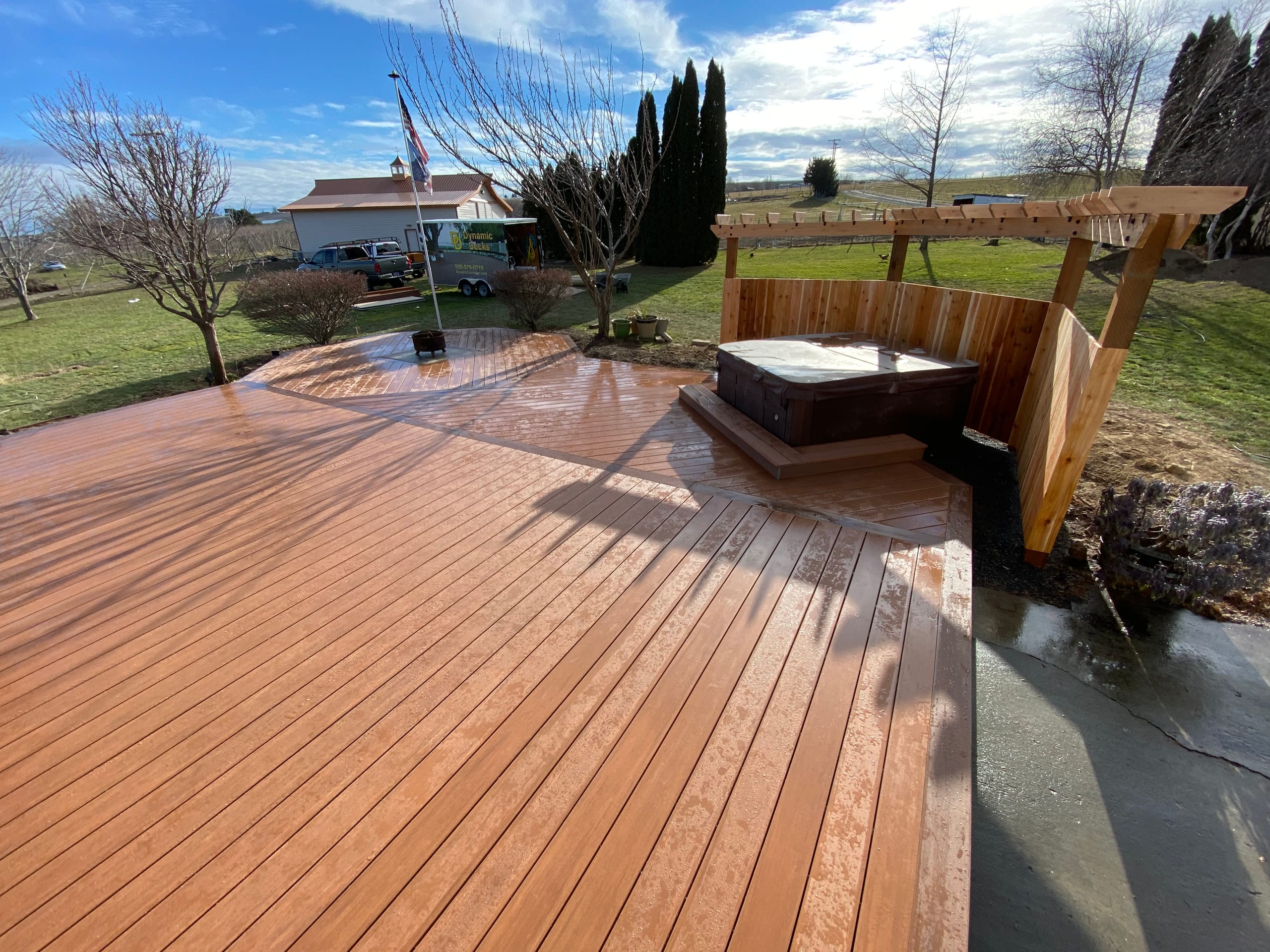 Wet reddish composite deck with cedar privacy pergola corner around hot tub, flag and open field