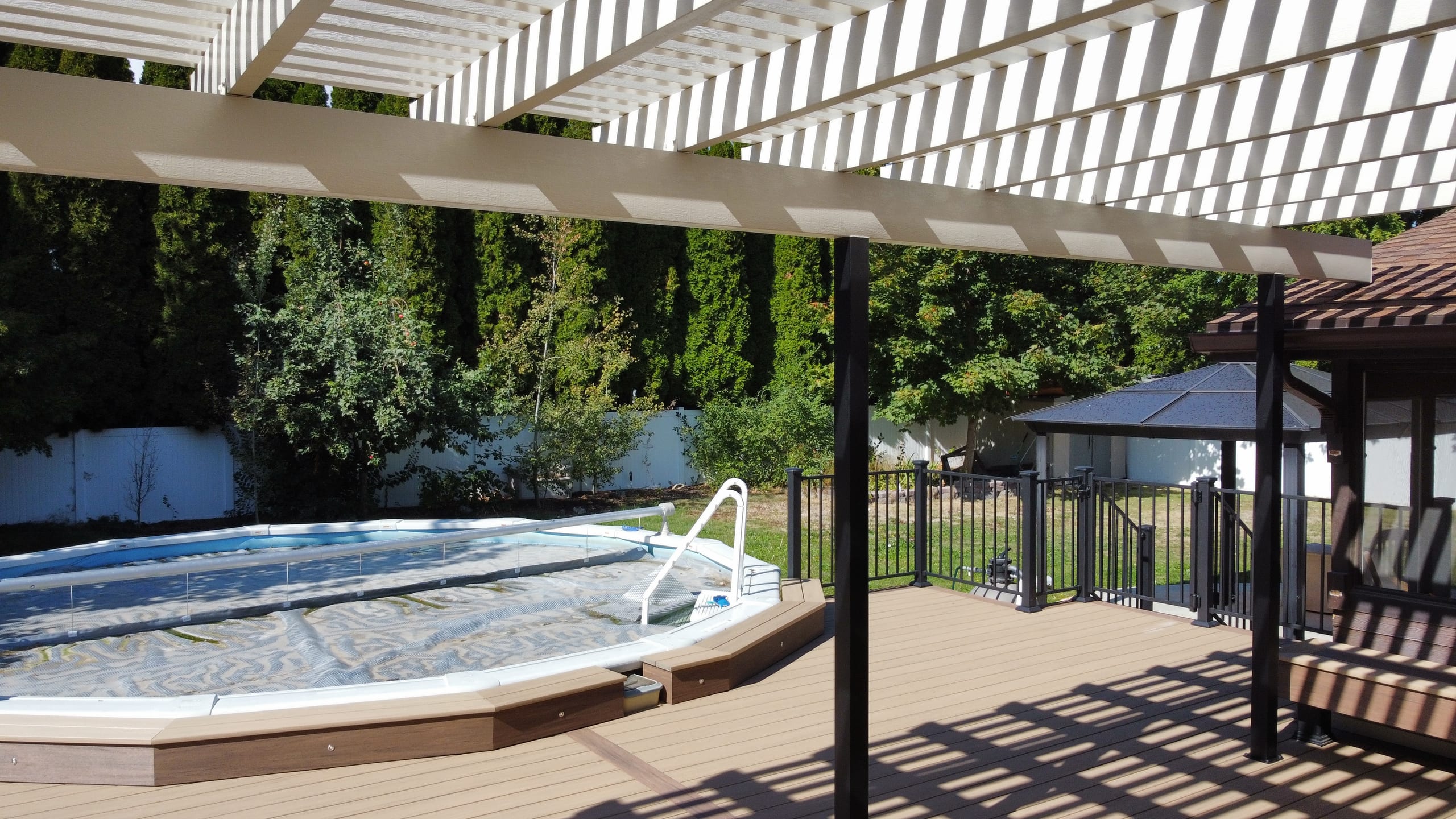 White louvered pergola over tan composite deck and sunken-style pool surround with black railing