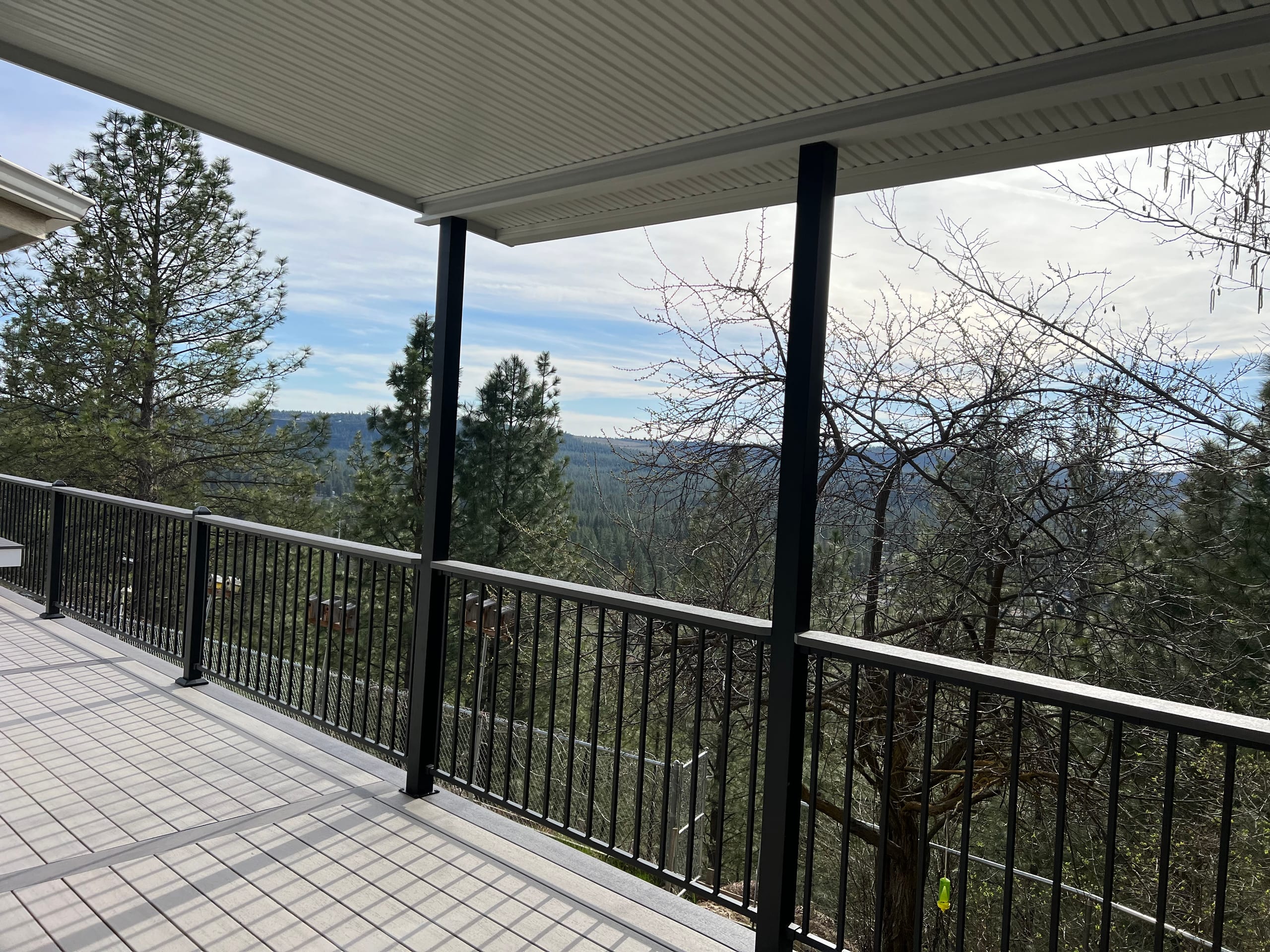 Wide covered grey composite deck with black posts and railing, scenic view across forested valley