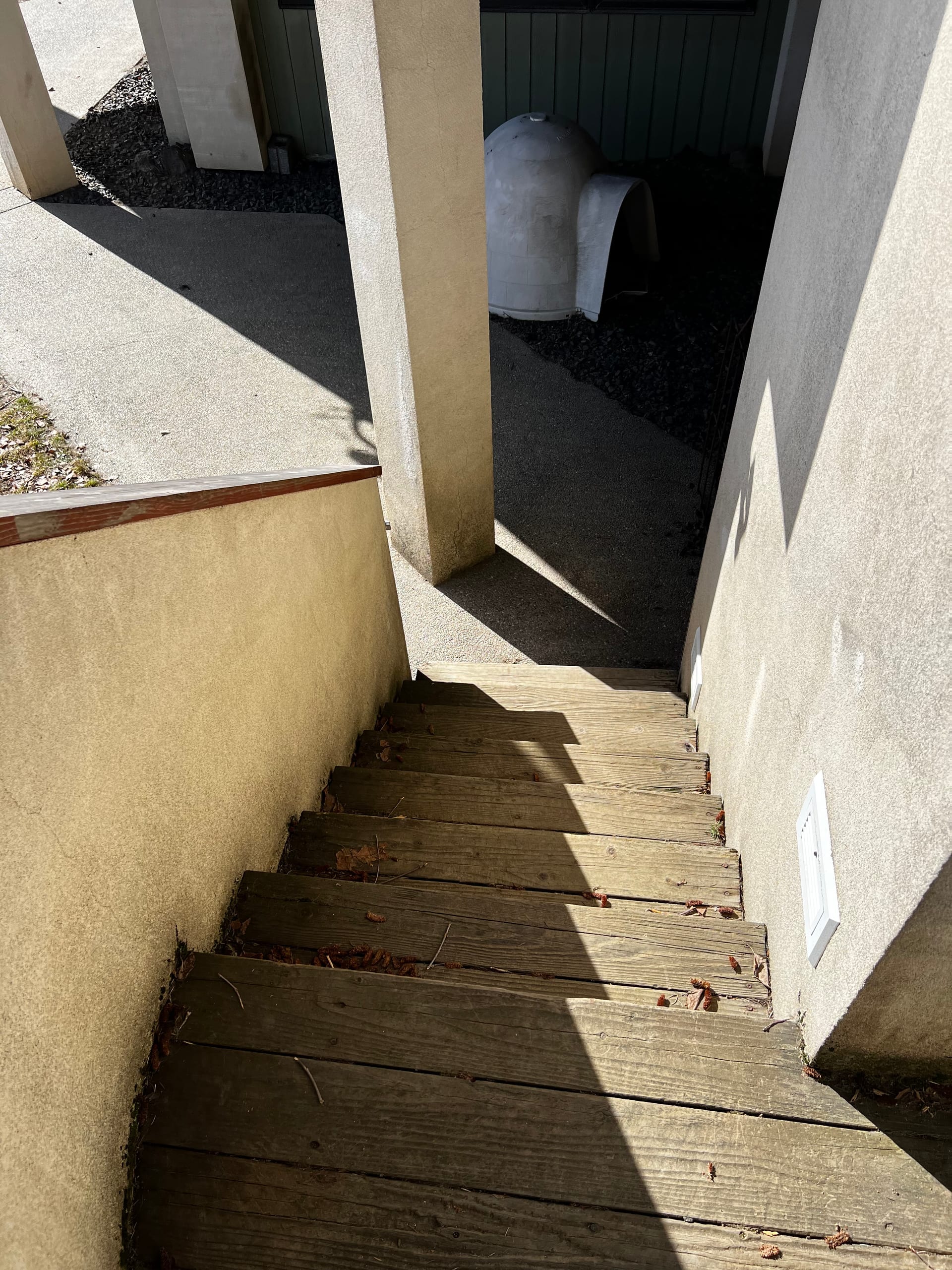 Worn wood stairs between stucco walls descending beside house, dog house shape below