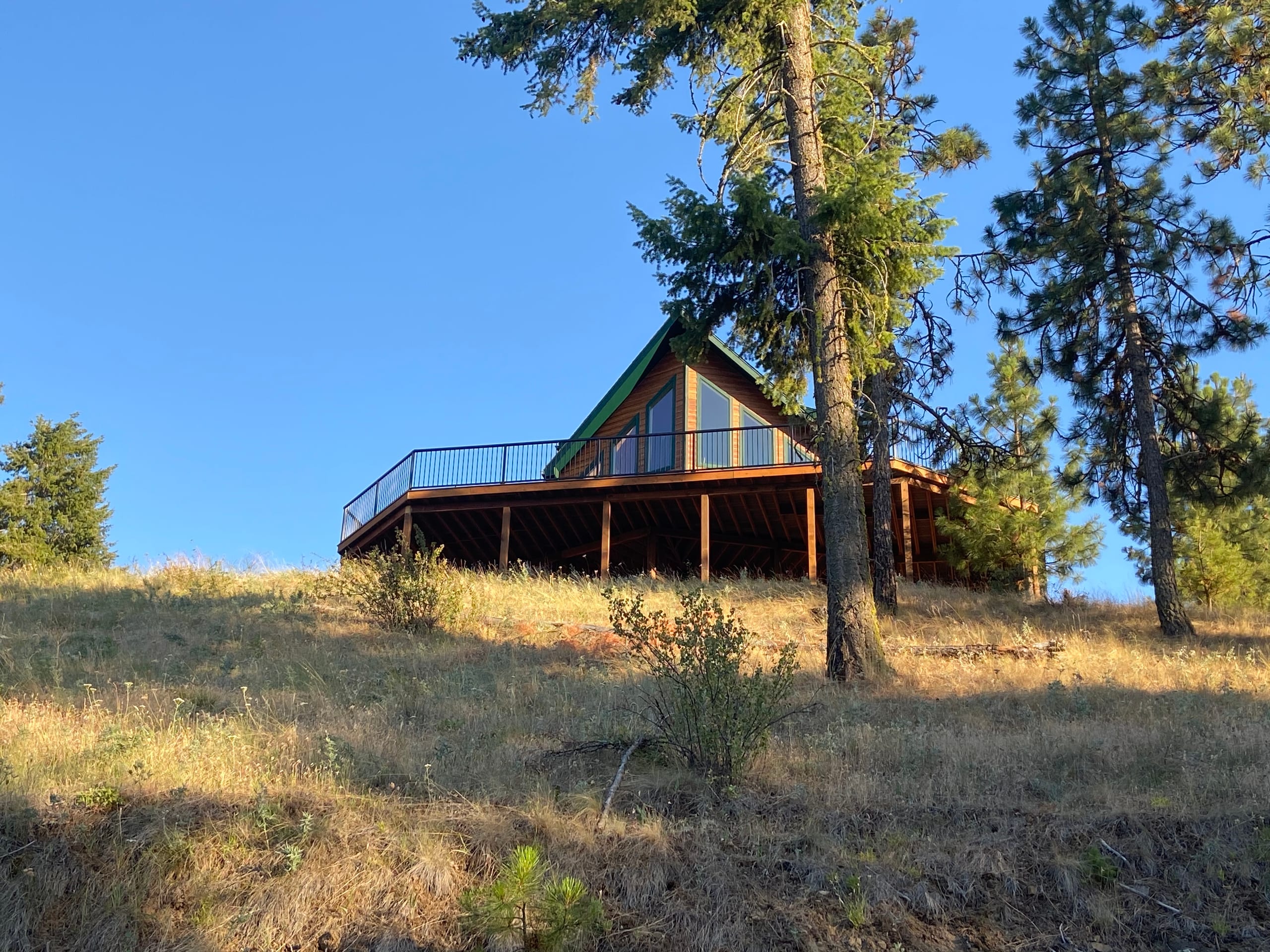 Wraparound elevated wood deck on an A-frame house on a grassy hillside, blue sky
